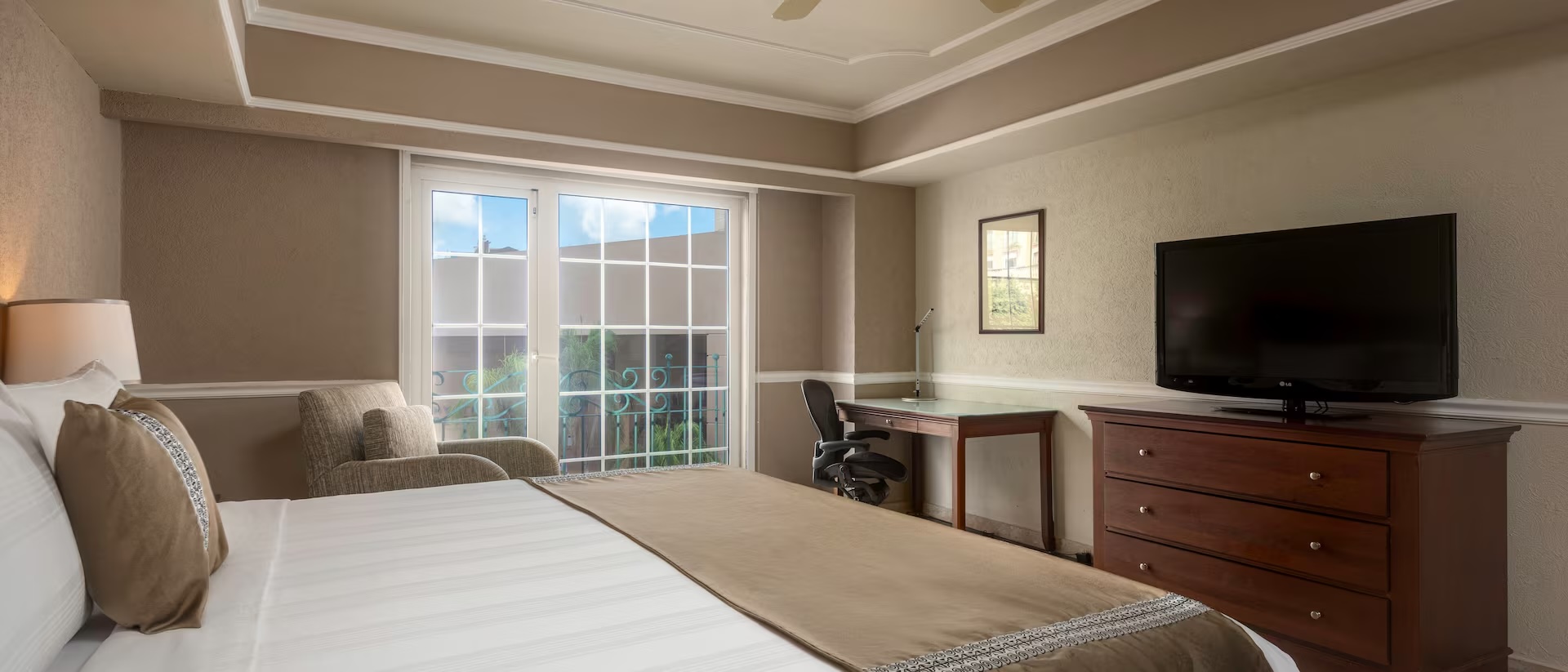 Comfortable MICE delegate accommodation at Villa Mercedes Mérida: Interior view of a king-sized guest room featuring contemporary furnishings, a comfortable bed, a dedicated desk/workspace for business travelers, and a large TV, ensuring a productive and restful stay for corporate groups and convention attendees.